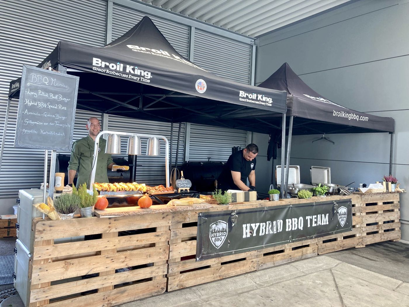 Grillstation unter Pavillons, dahinter Gäste an Stehtischen